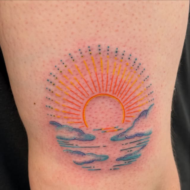 Colourful fine line sunset over ocean waves with clouds tattooed on the back of the leg