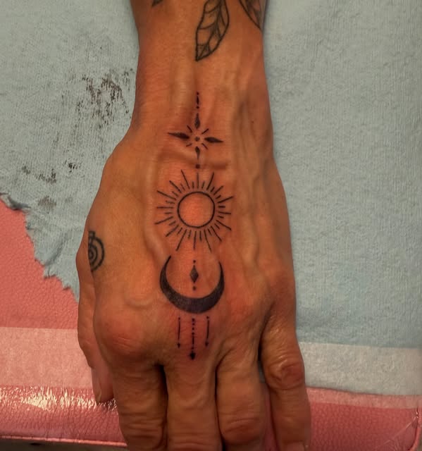 Fine line sun, moon and compass star tattooed down the back of a hand