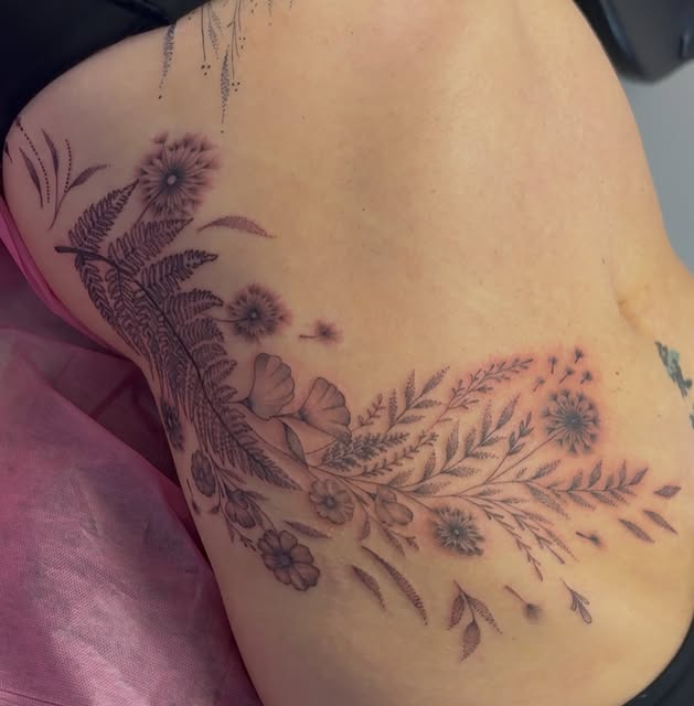 Fine line ferns and wildflowers flowing across the rib and hip