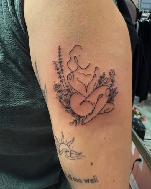 Fine line figure hugging her knees surrounded by flowers on the upper arm