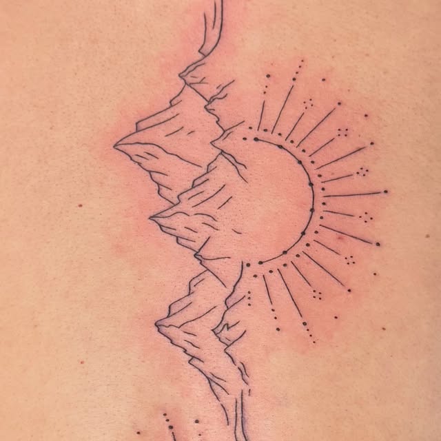 Close-up of a fine line sun and mountains tattoo along the spine
