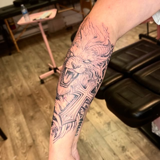 Black and grey lion with a cross starting a forearm sleeve