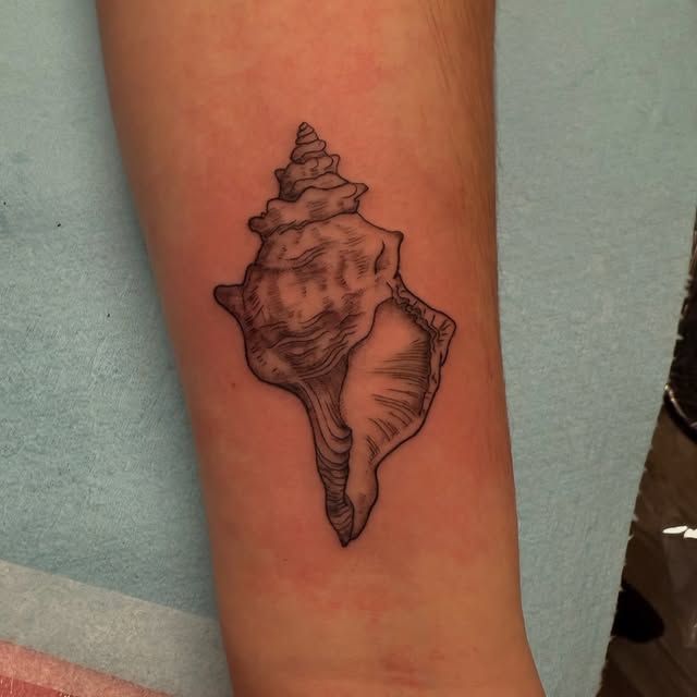 Shaded conch shell tattoo covering an old flame tattoo on the forearm