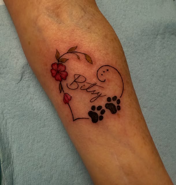 Heart with "Bitsy" script, red flowers and paw prints on the forearm