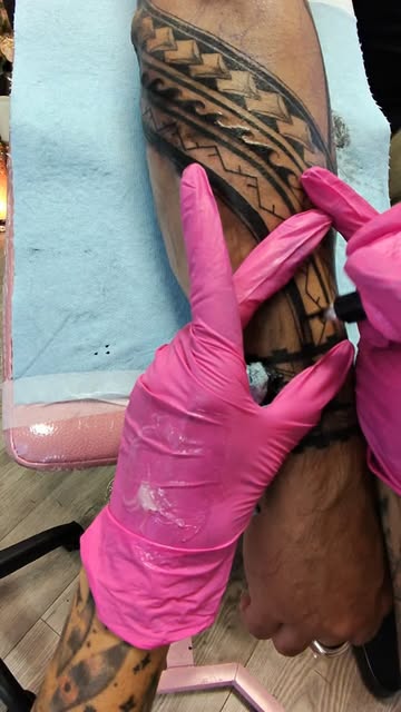 Lisa in pink gloves tattooing a Polynesian forearm sleeve