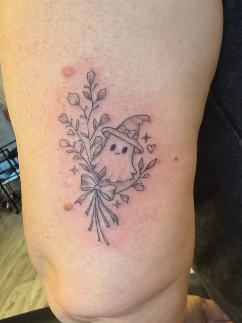 Fine line ghost in a witch hat with a flower bouquet on the upper arm
