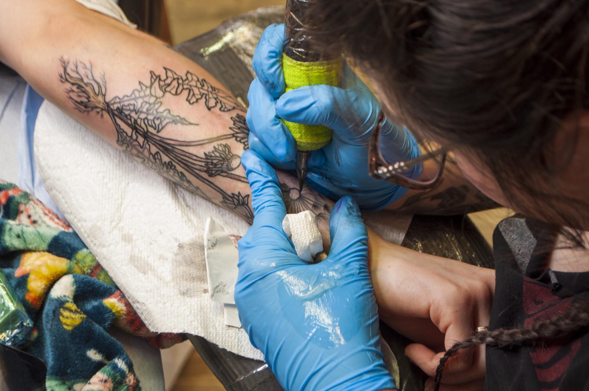Brynn adding fine line fern and botanical work to a forearm sleeve