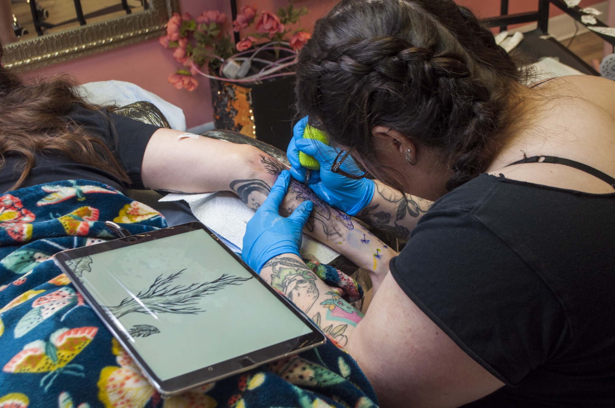 Brynn tattooing a botanical design with the drawing on an iPad beside her