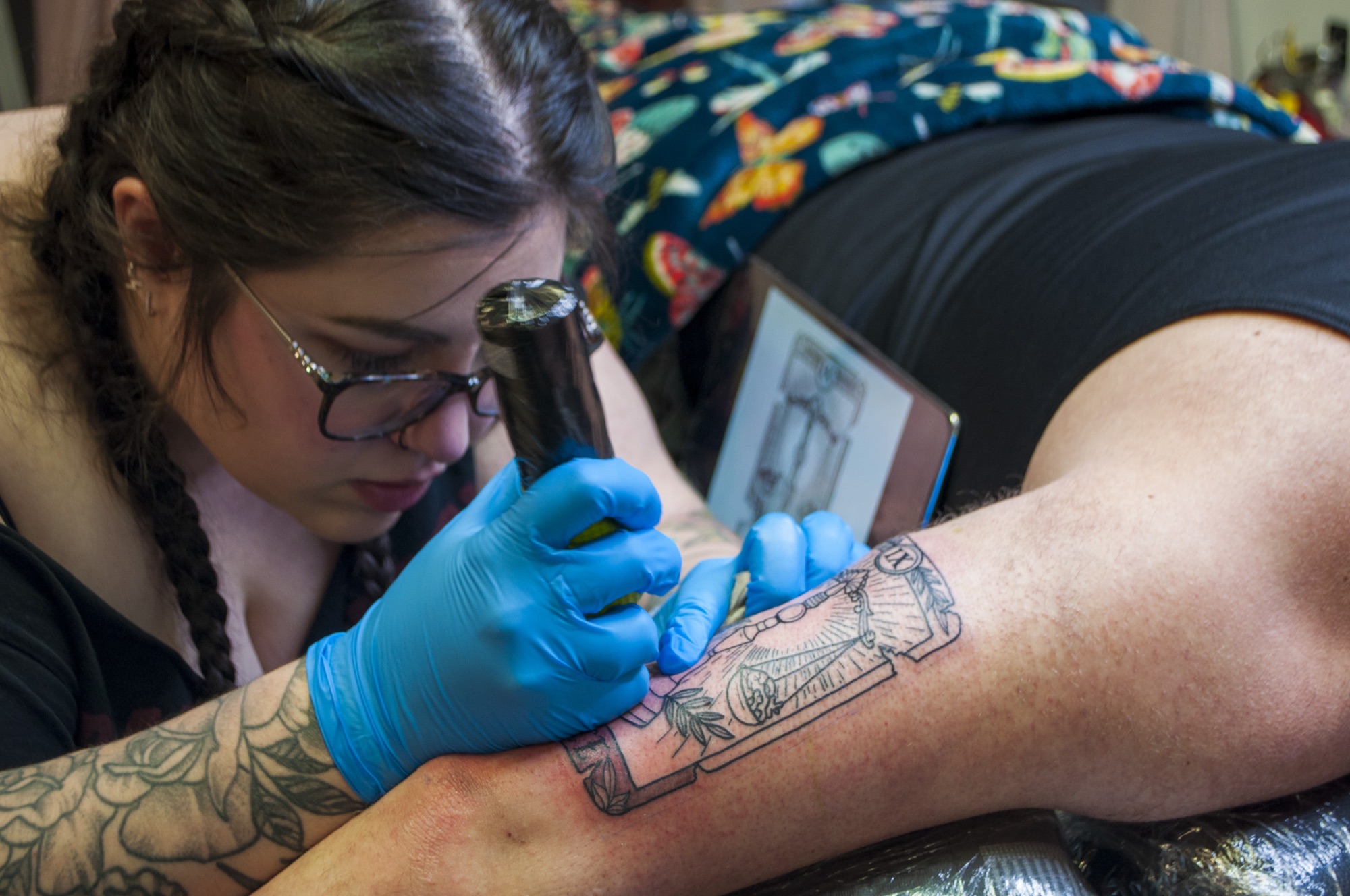 Brynn tattooing an illustrative framed piece on a client’s forearm