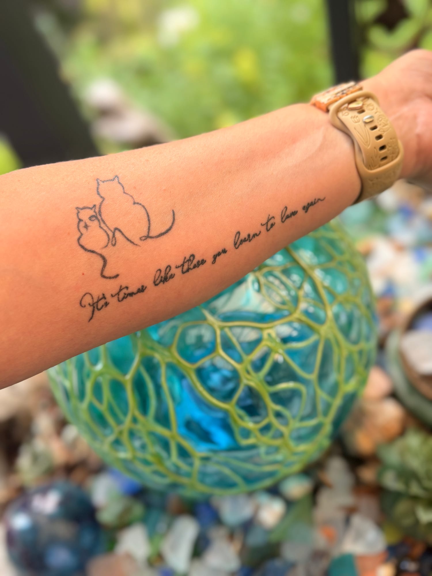 Fine line outline of two cats above flowing script on the forearm