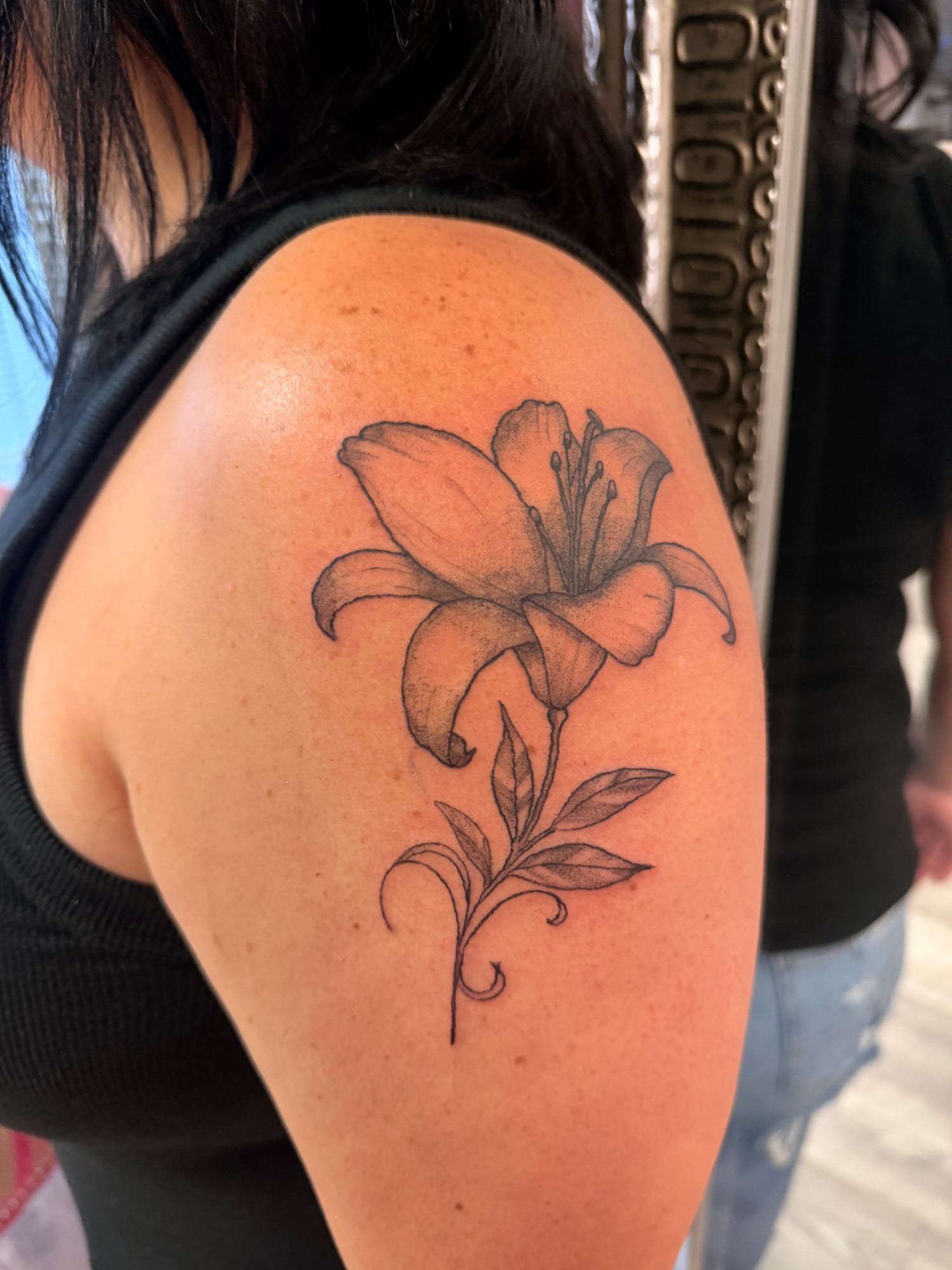 Black and grey lily with stippled shading and a curling stem on the shoulder
