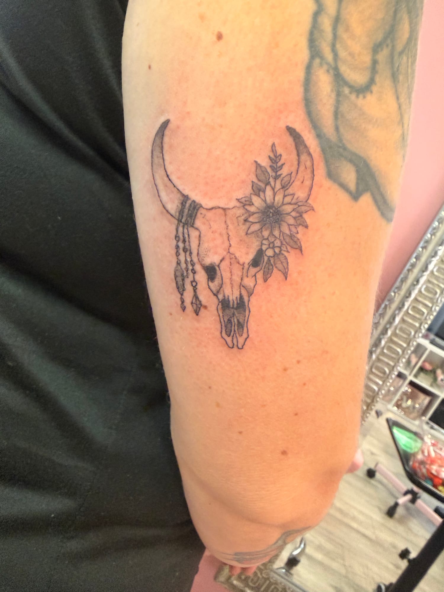 Fine line cow skull with a sunflower, leaves and beaded feather charms on the upper arm
